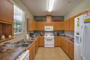 Interior Community Kitchen, Laminate countertops, brown cabinetry, tile floor, white appliances, dual stainless steel sink.