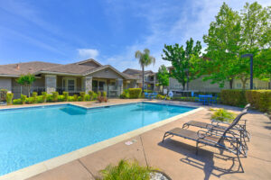 Exterior Community Pool, 2 chaise lounge chairs, palm tree planted in pool area, gated pool, two four seat picnic tables.